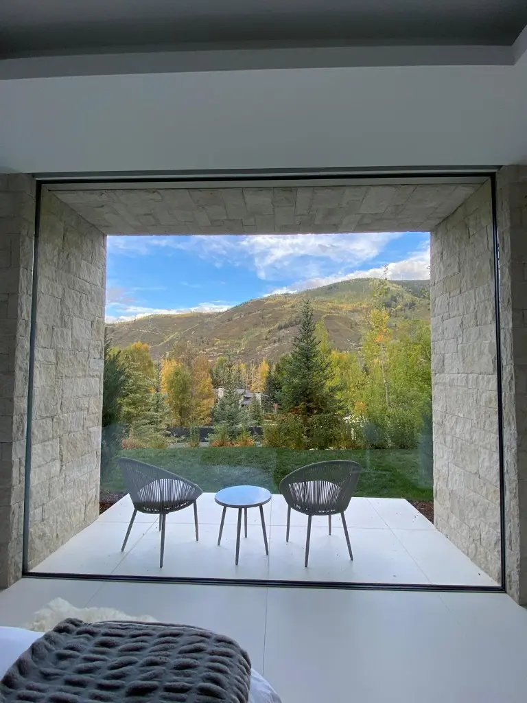 Two chairs on a terrace in front of a large opening onto a mountain view