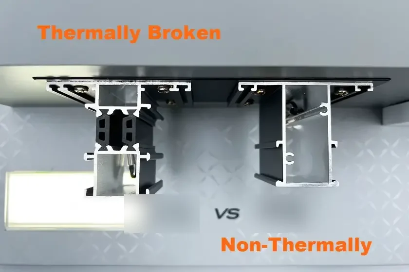Side-by-side cross-sections of a thermally broken aluminum frame with black insulating strips between two aluminum halves and a standard one-piece aluminum frame