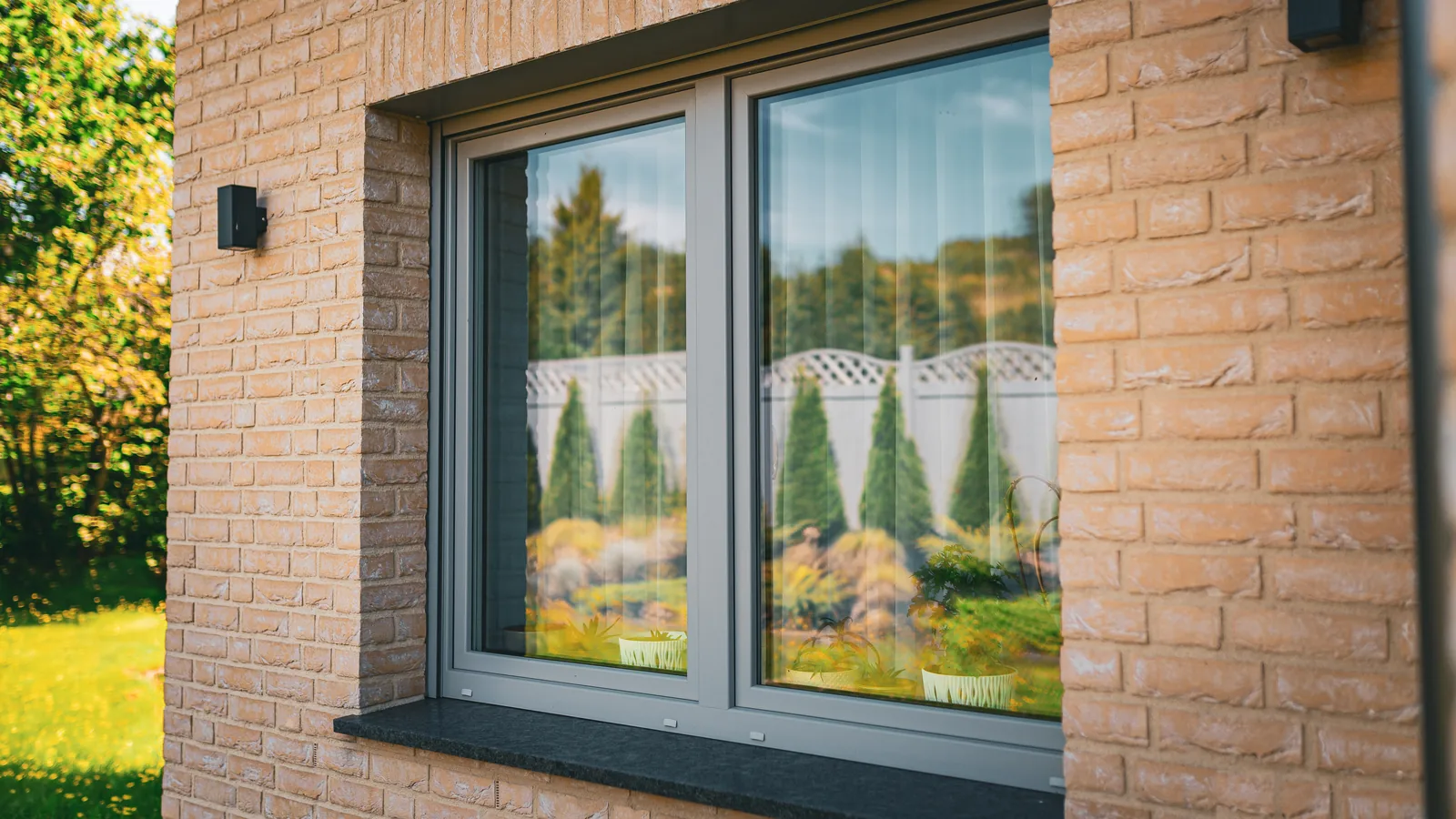 Grey uPVC double window in a light brick wall with a dark stone sill, reflecting a garden